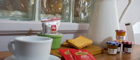 Una presentación de desayuno con una taza blanca, una taza verde, tostadas, frascos de mermelada y paquetes de té Twinings sobre una mesa de madera.