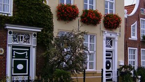 A building with a traditional facade, large windows, and flower boxes on the second floor. - Holiday home in the heart of Greetsiel with whirlpool, sauna, fireplace and garden (Greetsiel)