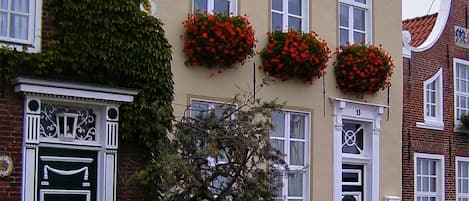 Un edificio con fachada tradicional, ventanas grandes y macetas con flores en el segundo piso.