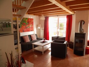 Una sala de estar acogedora con un sofá, una mesita de centro, una chimenea y un ventanal con cortinas rojas.