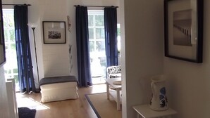 A room with a sofa, a small table, a chair, a floor lamp, and a vase on a side table. - Holiday home in the heart of Greetsiel with whirlpool, sauna, fireplace and garden (Greetsiel)