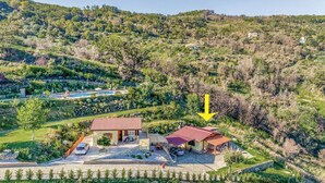 Una propiedad en una ladera con piscina, una casa de techo rojo y vistas del paisaje circundante.