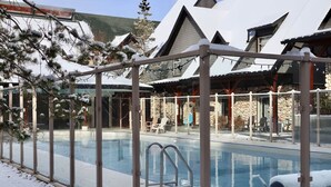 Ein Poolbereich mit Glasveranda, Liegestühlen und einem Steinhaus im Hintergrund.
