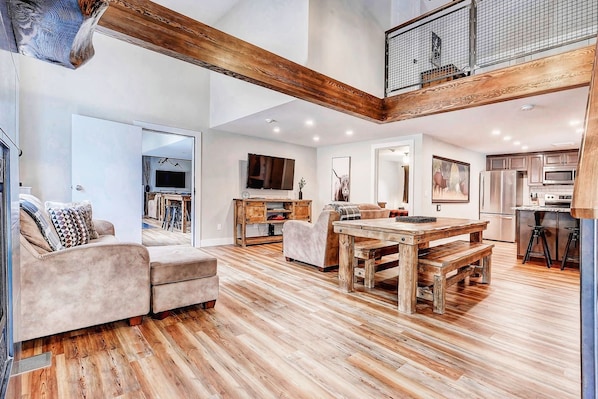 A spacious living area with a wooden dining table, sofas, and a kitchen in the background.
