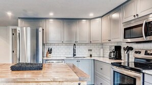 Eine moderne Küche mit weißen Schränken, Edelstahlgeräten und einem Holztisch.