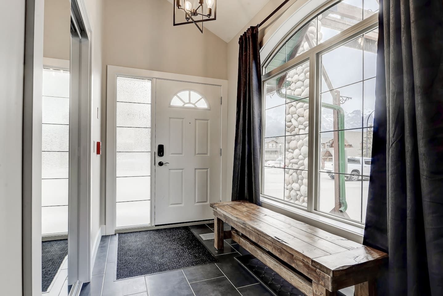 Un couloir avec un banc, une porte blanche et une grande fenêtre avec des rideaux.