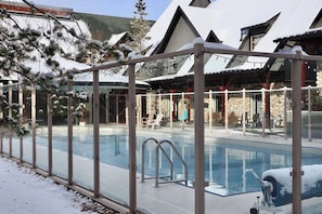 A pool area with a glass enclosure, lounge chairs, and a stone building in the background.