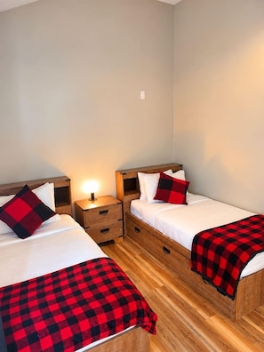 A room with two beds, each with a wooden headboard, a bedside table, and a lamp.