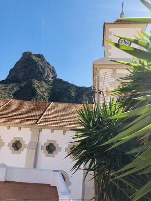 A building with a clock tower, a tiled roof, and a mountain in the background. - The House of Telegraphs (Vallehermoso)