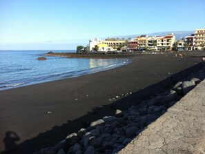 A beach with a rocky shoreline and buildings in the background. - The House of Telegraphs (Vallehermoso)