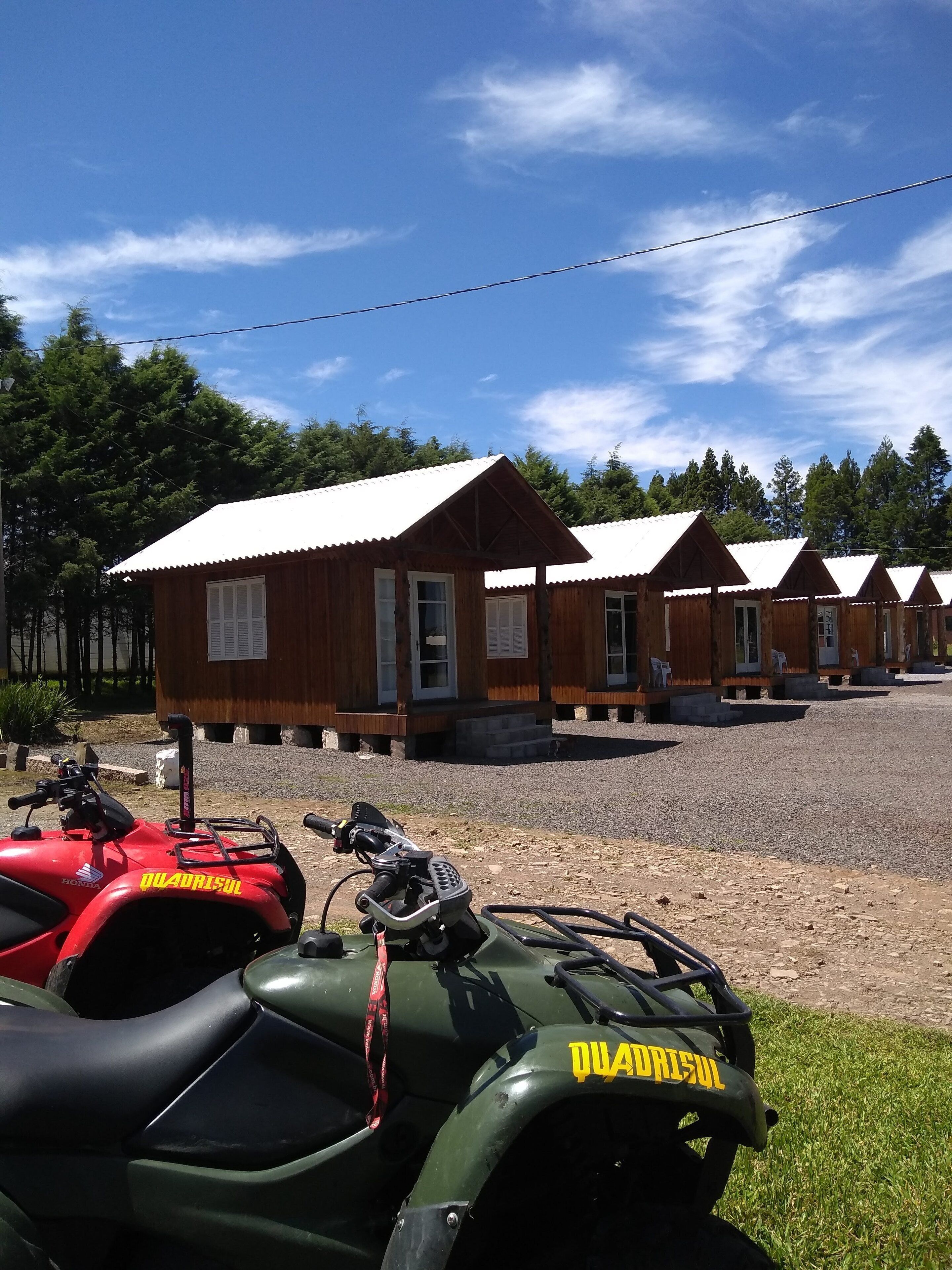 Uma fileira de cabanas de madeira com telhados de metal, um estacionamento de brita e duas motocicletas quadriciclo estacionadas na frente.