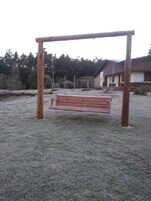Un conjunto de columpios de madera en un césped, con un edificio al fondo.