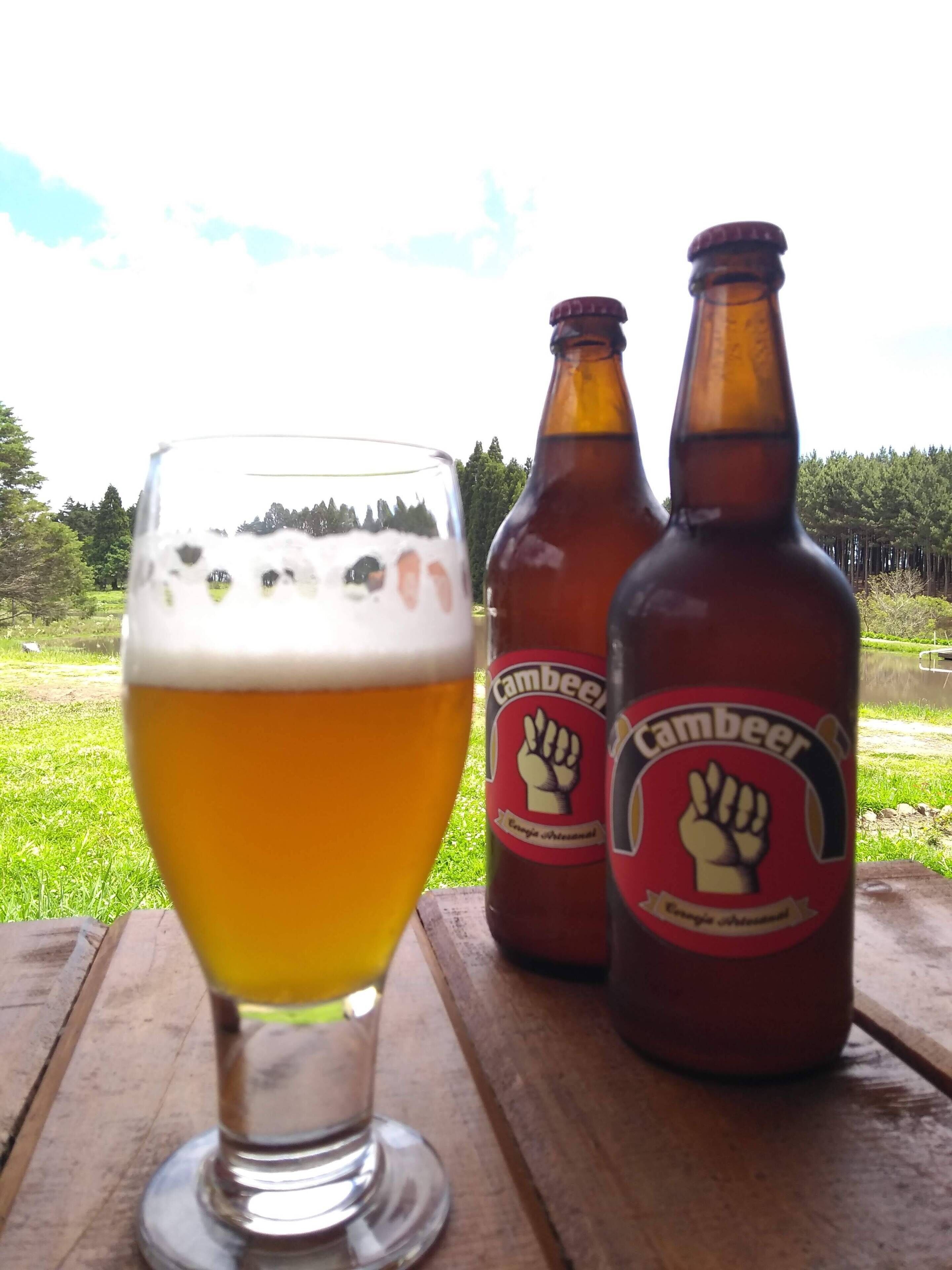 Una cerveza con dos botellas de Cambeel sobre una mesa de madera.