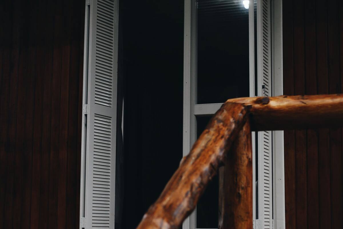 A wooden railing with a window in the background.