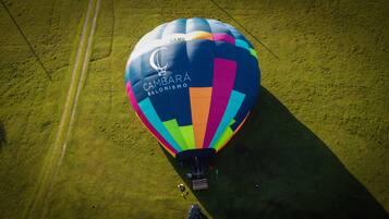 A colorful hot air balloon with "CAMPBARA BALONISMO" text, parked on a grassy field with a clear sky.