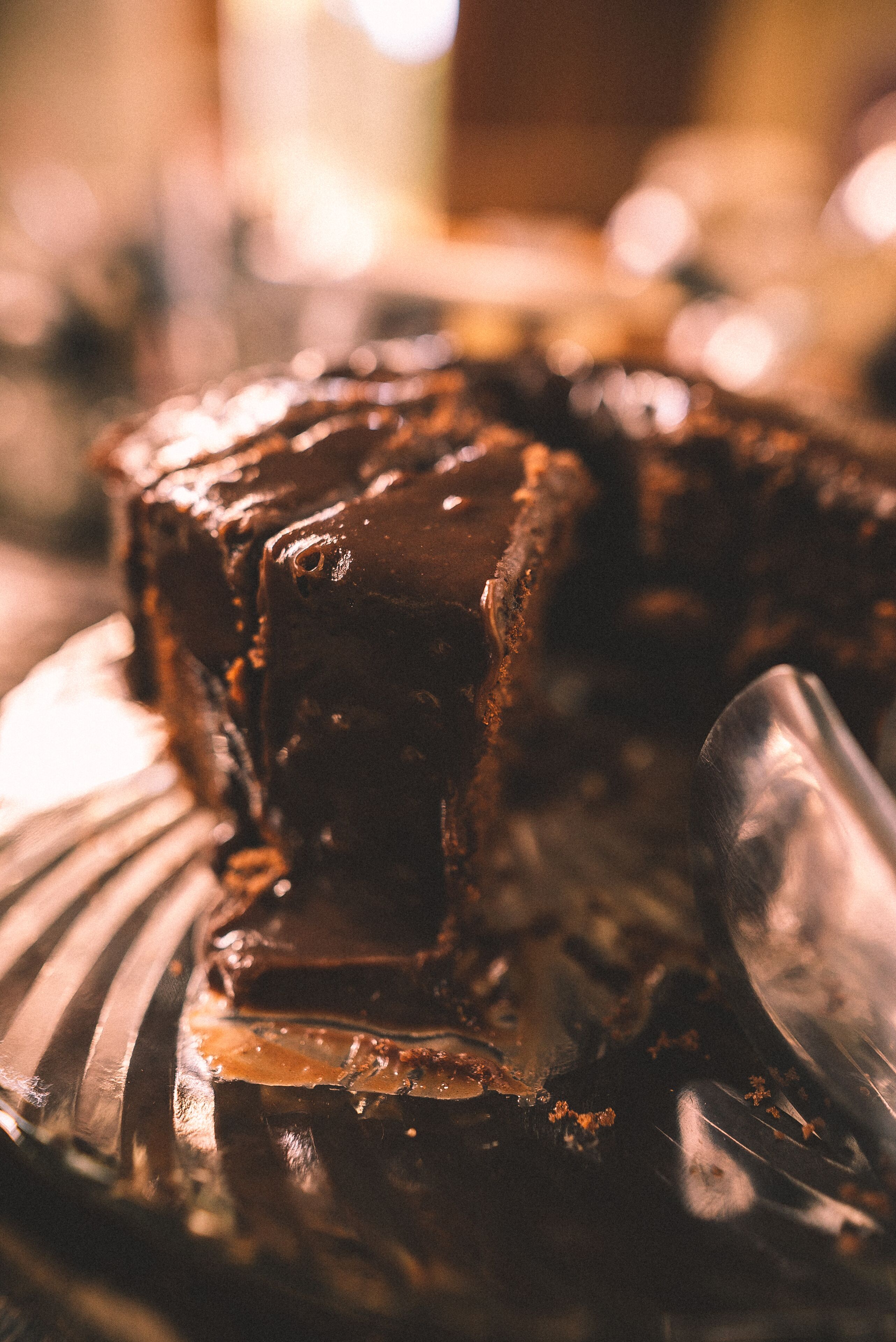 A close-up of a chocolate dessert with a glossy finish, possibly a cake or tart, on a plate with a spoon beside it.