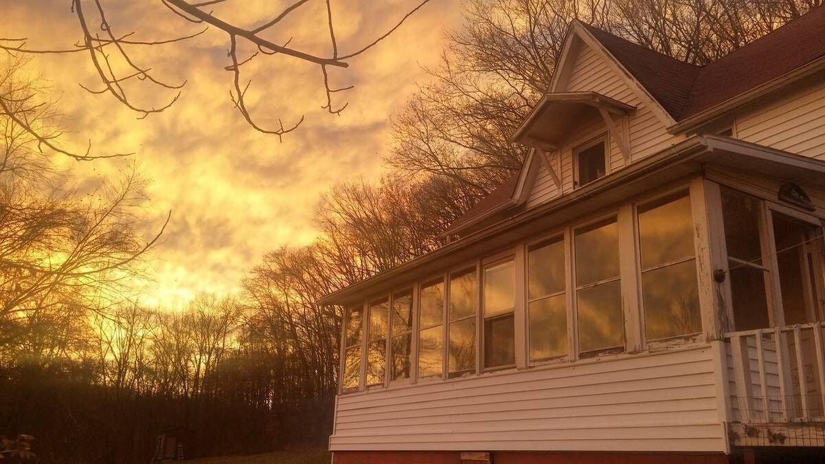 Ein zweigeschossiges Haus mit einem großen Erkerfenster, umgeben von Bäumen und einem bewölkten Himmel.