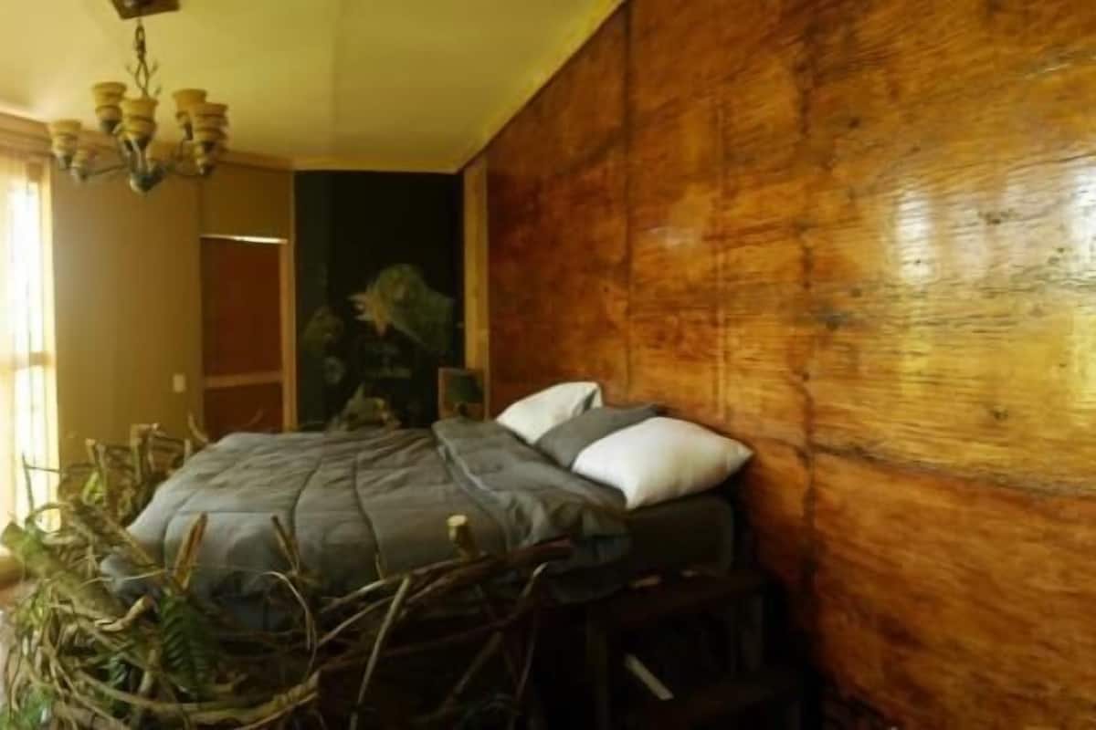 A bedroom with a bed, wooden walls, and a large window with curtains.