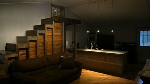 A modern living room with a wooden staircase, a sofa, and a kitchen area with a bar. - Lost River Hostel (West Baden Springs)