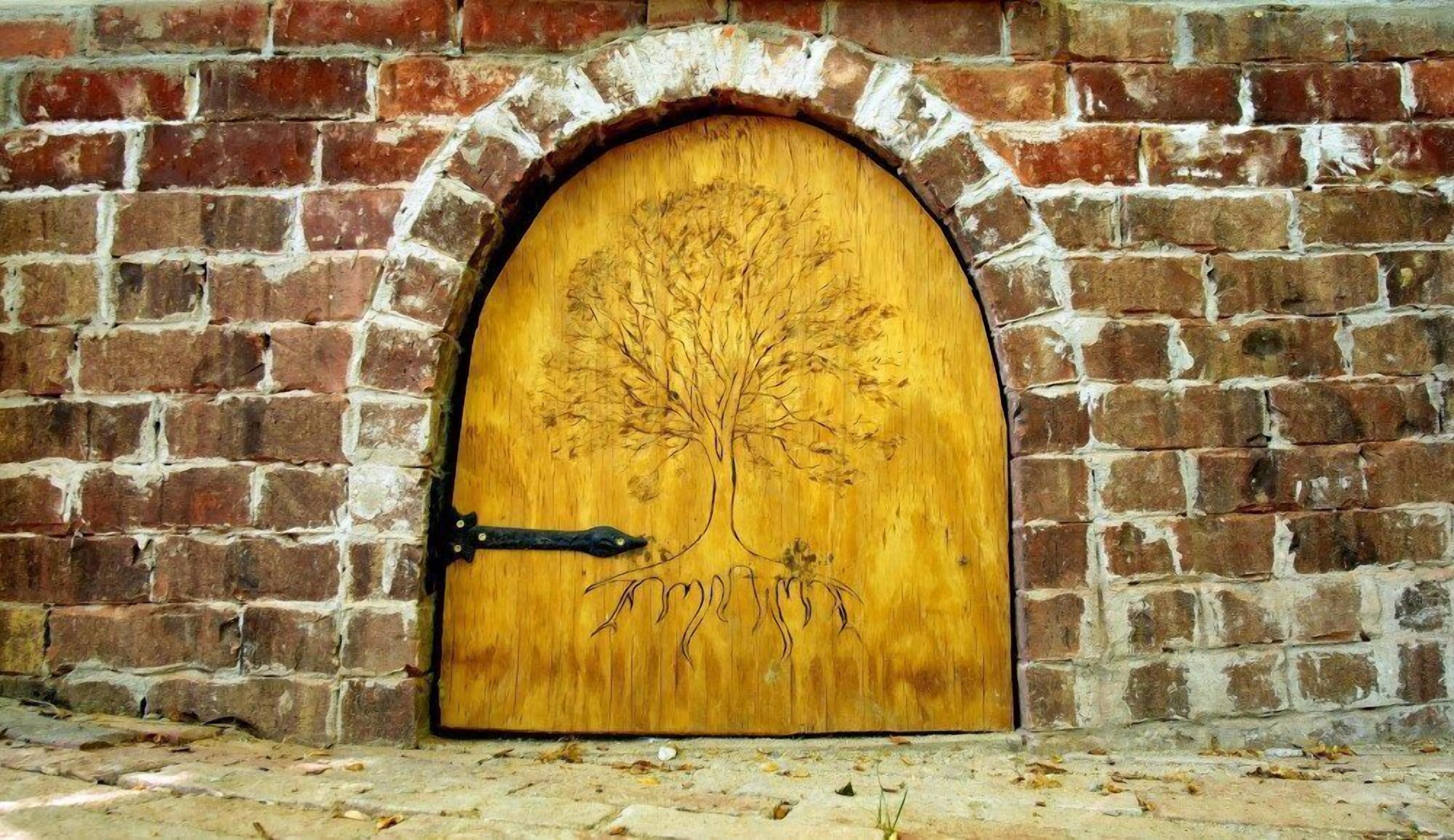 Une porte en bois ornée d’une sculpture représentant un arbre, encastrée dans un mur de briques.