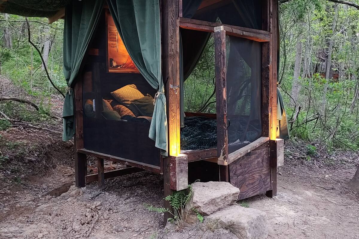 A rustic wooden cabin with a bed, curtains, and a window.