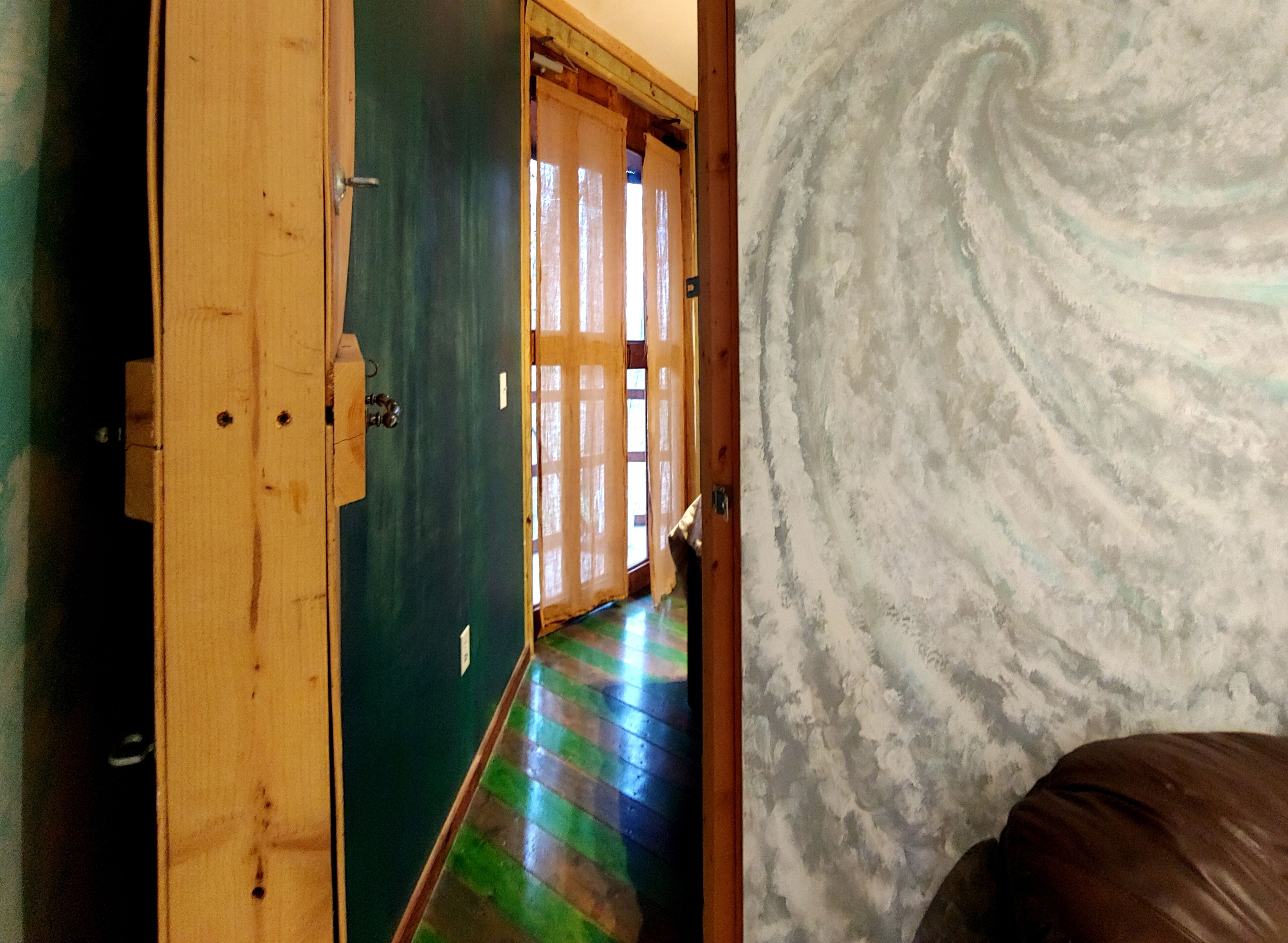 Un pasillo con puerta de madera, pared verde y suelo estampado.