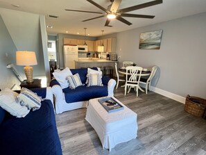 A living room with a blue sofa, white ottoman, and a ceiling fan.