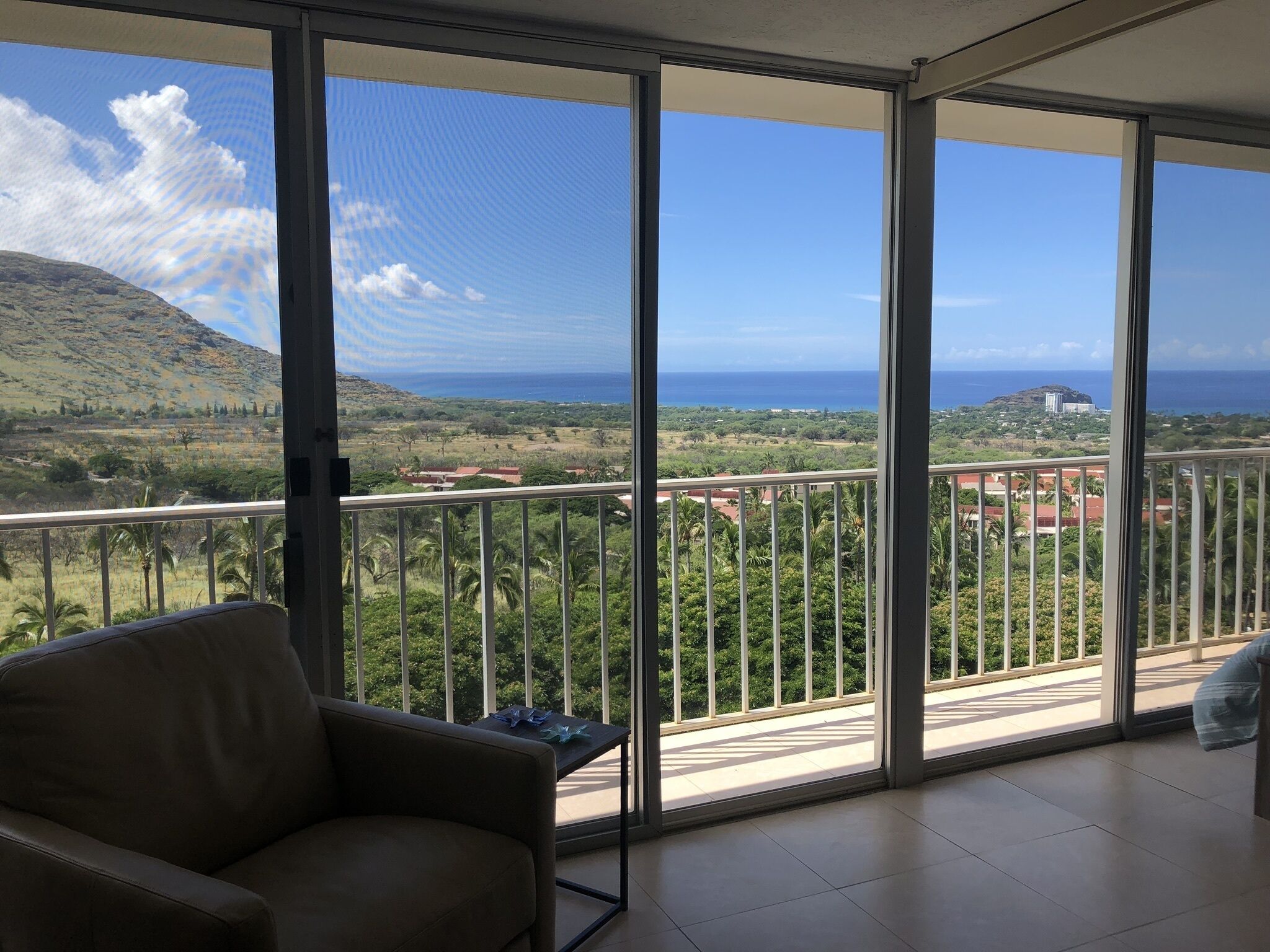 A balcony with a view of a coastal landscape, including a hill and the ocean.