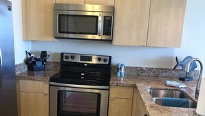A kitchen with stainless steel appliances, wooden cabinets, granite countertops, and a tiled floor. - Beautiful Condo located at Makaha Valley Towers (Waianae)