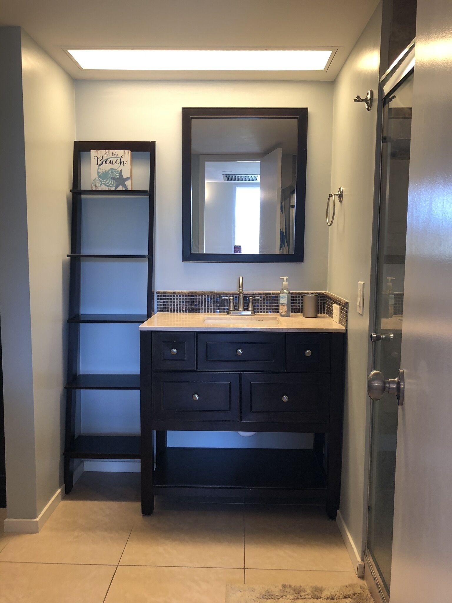 A bathroom with a dark vanity, a mirror, and a shelf with a 'Beach' sign.