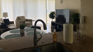 A modern living room with a sofa, a TV, a dining area with a table, and a kitchen with a sink and countertop. - Beautiful Condo located at Makaha Valley Towers (Waianae)