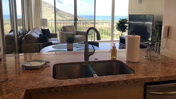 A kitchen with a granite countertop, stainless steel sink, and a dining area with a table and chairs. - Beautiful Condo located at Makaha Valley Towers (Waianae)