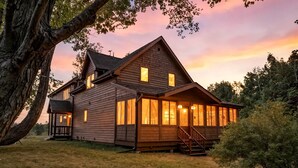 A large wooden house with multiple windows and a porch, surrounded by trees.