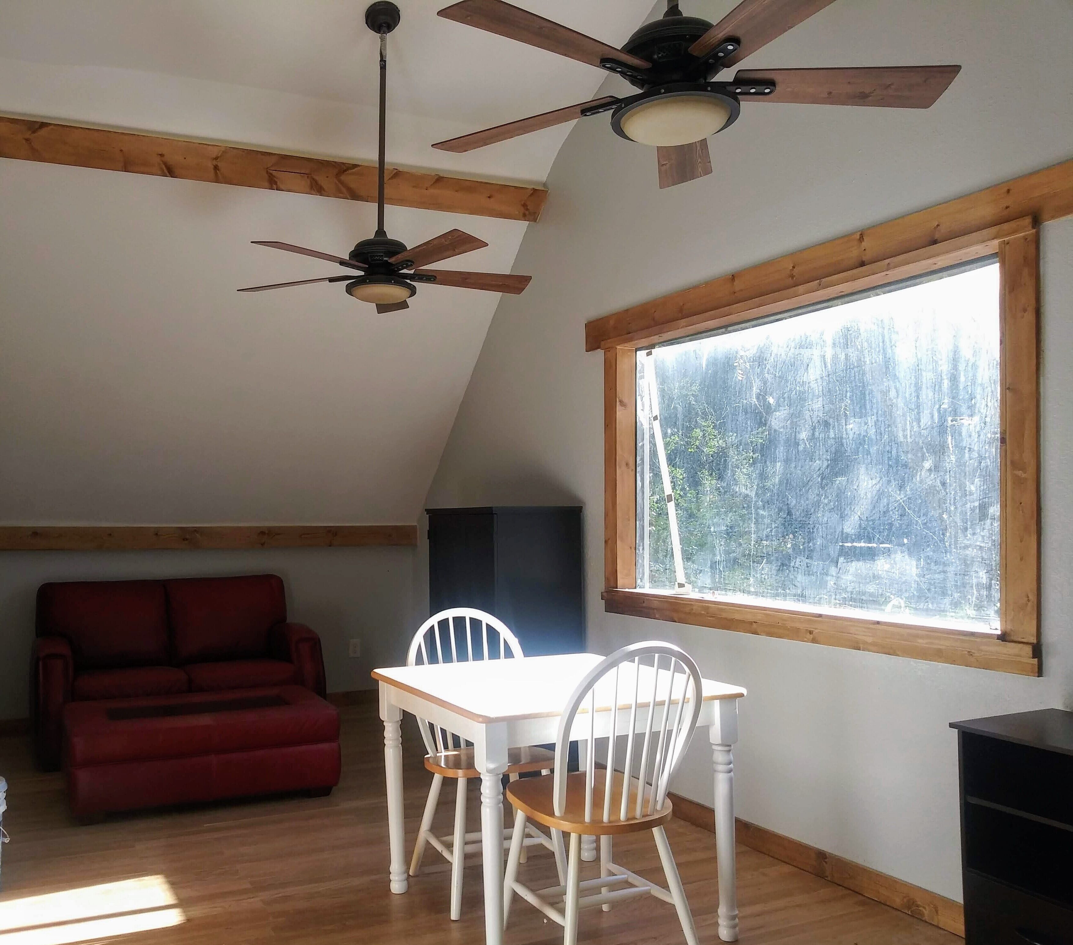 Une pièce comprenant une table à manger et des chaises, un canapé rouge et deux ventilateurs de plafond.