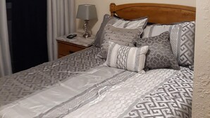 Una cama bien hecha con ropa de cama estampada, cabecera de madera y un cuadro de flores colgado en la pared.