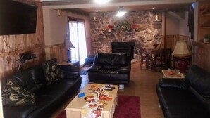 Una sala de estar con pared de piedra, dos sofás de cuero negro, una mesa de centro de madera y un ventilador de techo.
