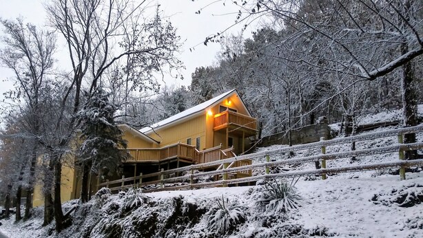 Una cabaña de madera con balcón, rodeada de árboles cubiertos de nieve y una valla de madera.