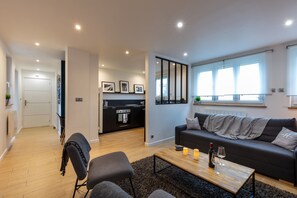 Un salon moderne avec un canapé, une table basse et des fauteuils. Il y a également un coin cuisine équipé d’une cuisinière et d’un réfrigérateur.