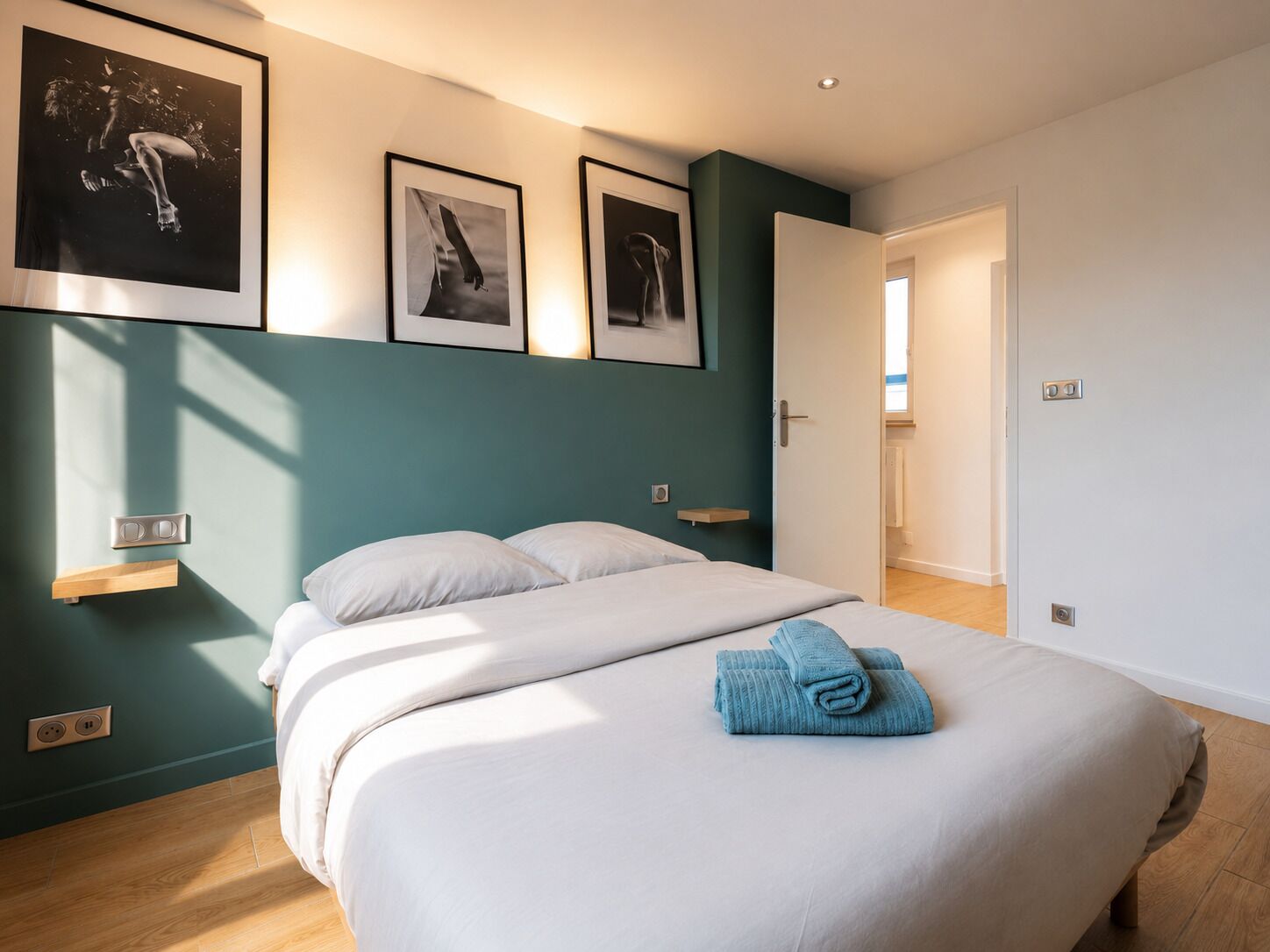 Ein Schlafzimmer mit Bett, Nachttisch, Wandleuchte und einer Tür zu einem anderen Raum.