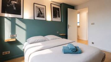 A bedroom with a bed, a nightstand, a wall-mounted light, and a door leading to another room.