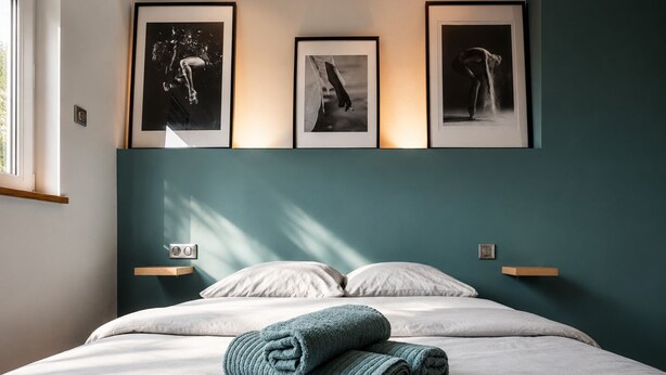 Une chambre d’hôtel avec un lit, deux oreillers, une serviette pliée et trois photographies encadrées accrochées au mur.