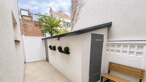 Un petit espace extérieur avec un banc, une porte et trois jardinières fixées au mur.