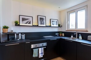 Une cuisine moderne avec des meubles de couleur noire, un four à micro-ondes, un évier et une fenêtre.