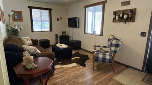 A living room with a brown sofa, a plaid armchair, a wooden coffee table, and a television mounted on the wall. - Bungalow on a private 70 acre ranch (Austin)