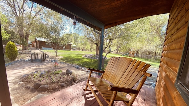 A wooden rocking chair on a porch with a view of a backyard, a wooden cabin, and a swing set. - Bungalow on a private 70 acre ranch (Austin)