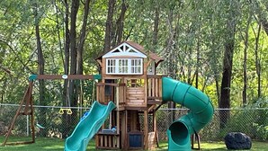 A wooden playhouse with a slide and a swing set in a grassy area. - Bungalow on a private 70 acre ranch (Austin)