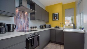 A modern kitchen with grey cabinets, a white countertop, and a yellow accent wall.