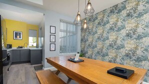 A modern kitchen with a wooden dining table and bench, a yellow accent wall, and a textured wall behind the table.