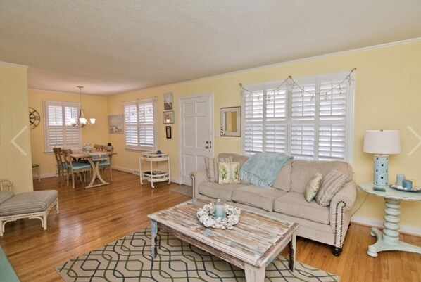 A living room with a beige sofa, a coffee table, and a dining area with a table and chairs.