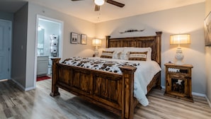 Un dormitorio con cama de madera, ventilador de techo, lámparas de noche y una mesita de noche pequeña.